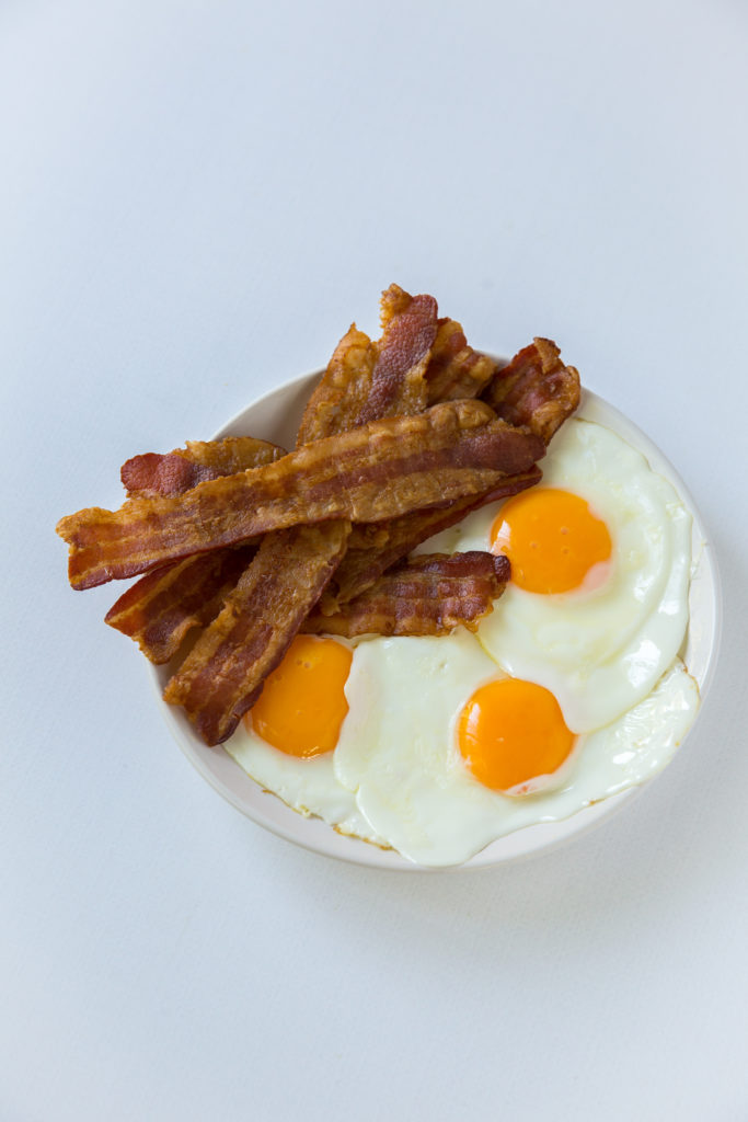 A white plate with lots of bacon and three sunny side up eggs