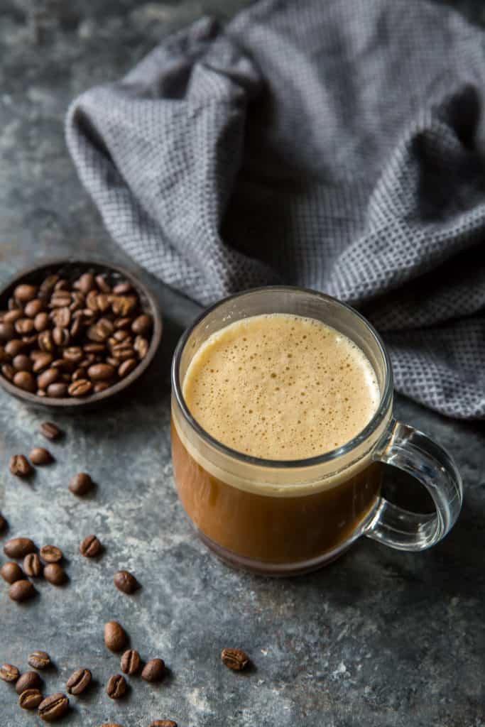 Bulletproof Coffee coffee in a clear cup with a bowl of coffee beans in the background