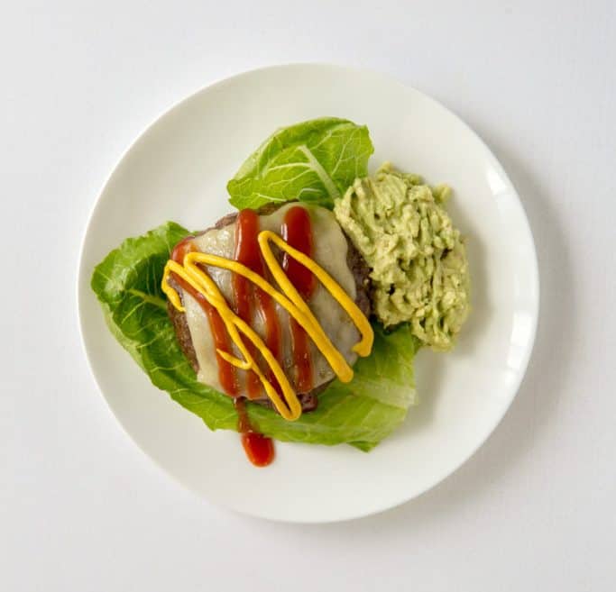 A cheeseburger with mashed avocado over romaine. 