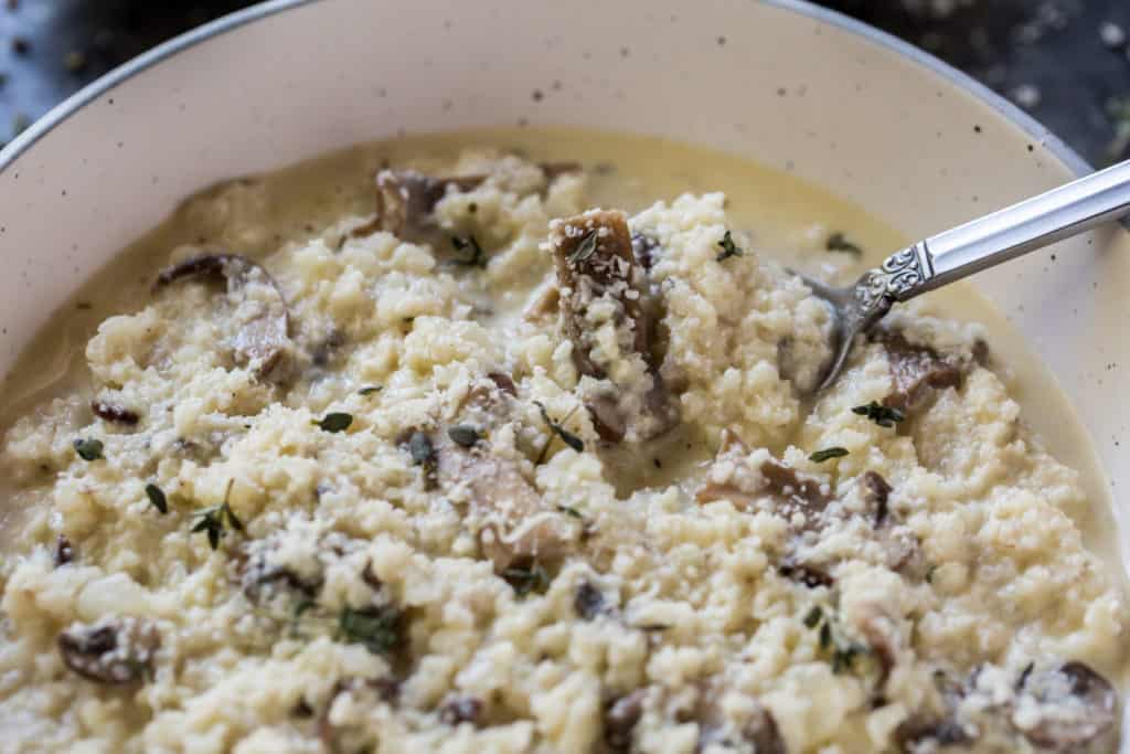 cooked cauliflower risotto in a white bowl with a spoon