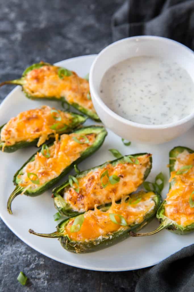six cooked air fryer jalapeno poppers on a white plate with a side of blue cheese dressing in a white bowl