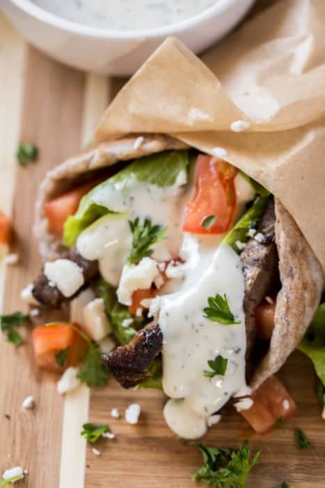 one healthy gyros recipe wrapped in parchment paper and topped with tzatziki sauce