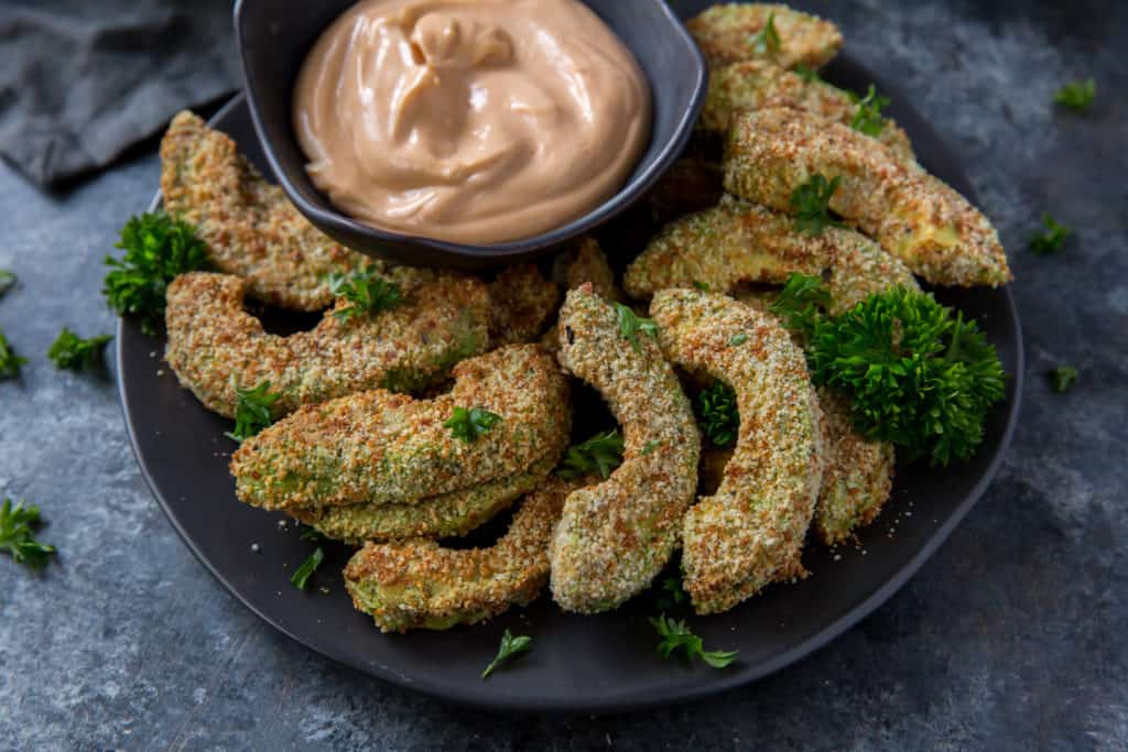 air fryer avocado fries served on a black plate with a dipping sauce