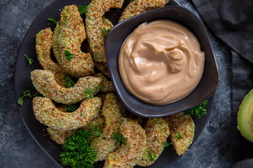 air fryer avocado fries served on a black plate with parsley garnish and a dipping sauce