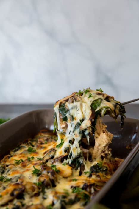 Keto Chicken Casserole baked keto chicken casserole in a gray casserole dish with spoon scooping out a serving of casserole