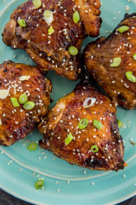 Air fryer chicken thighs on a blue plate garnished with scallions and sesame seeds