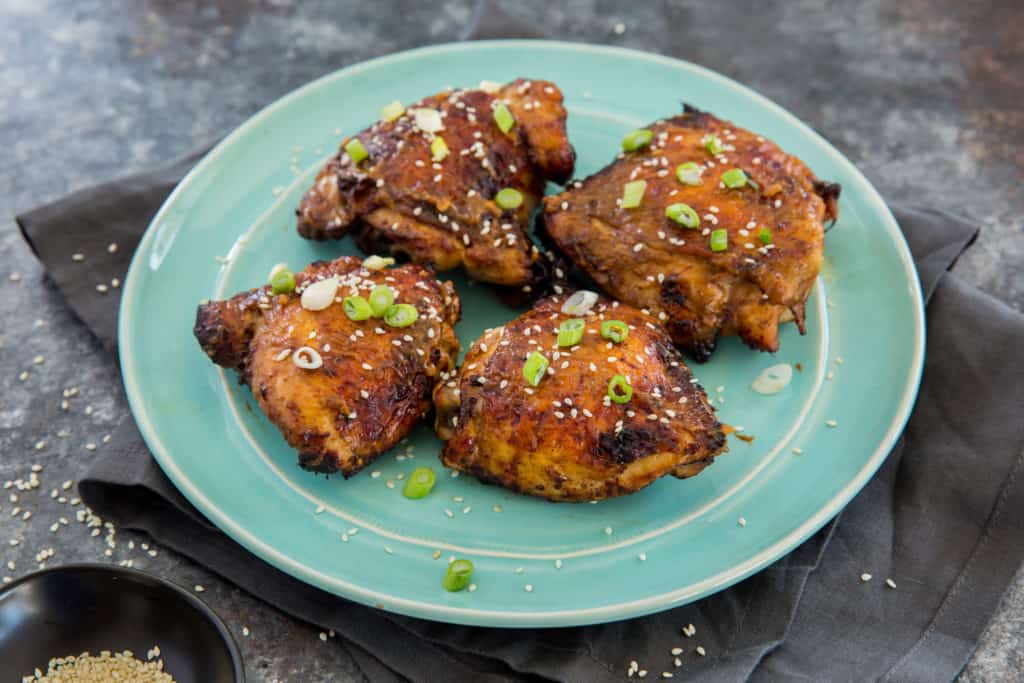 Air fryer chicken thighs on a blue plate topped with scallions and sesame seeds.