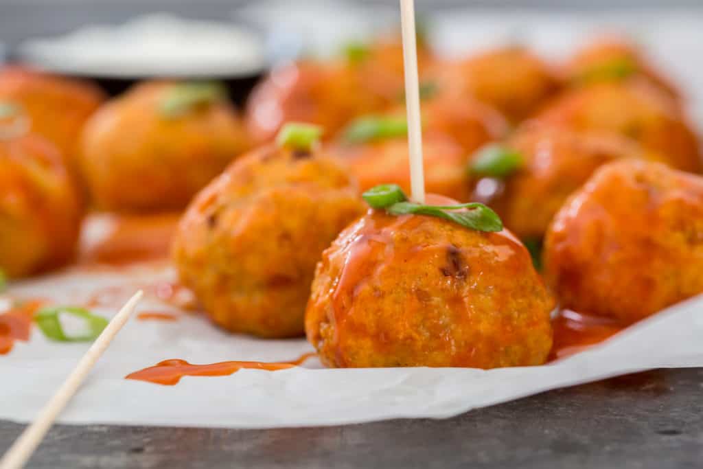 Buffalo chicken meatballs on parchment paper with a toothpick in one of the meatballs and garnished with scallions