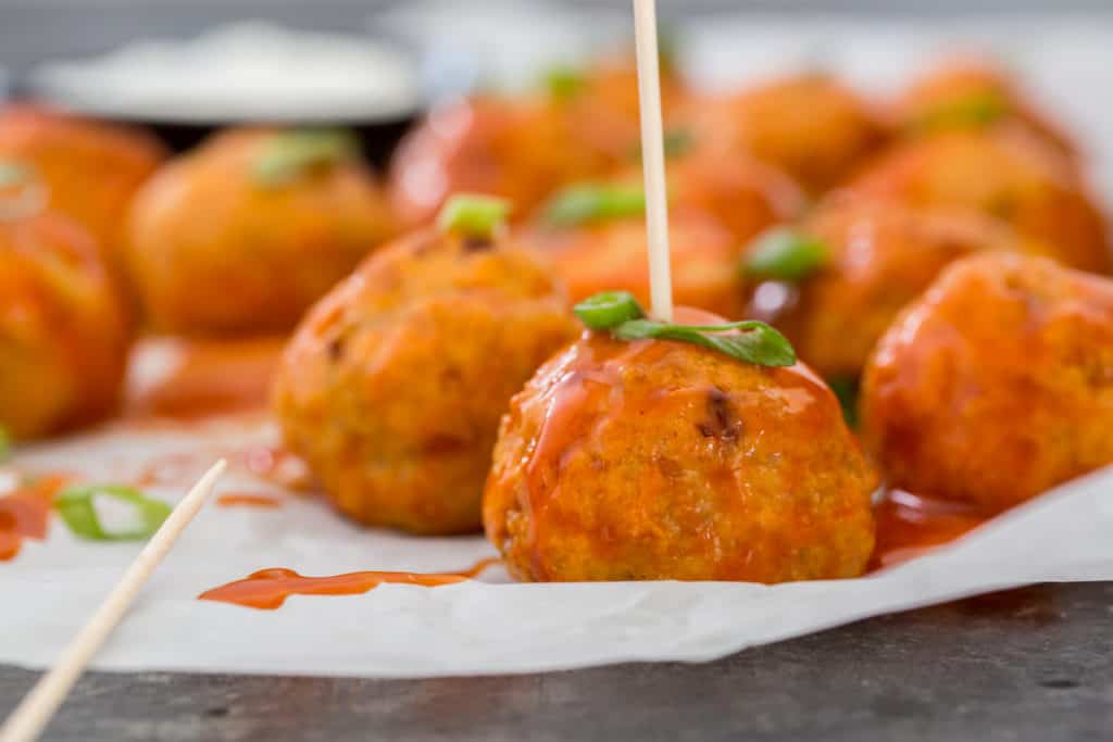 best keto chicken recipes buffalo chicken meatballs on parchment paper being pierced with a toothpick