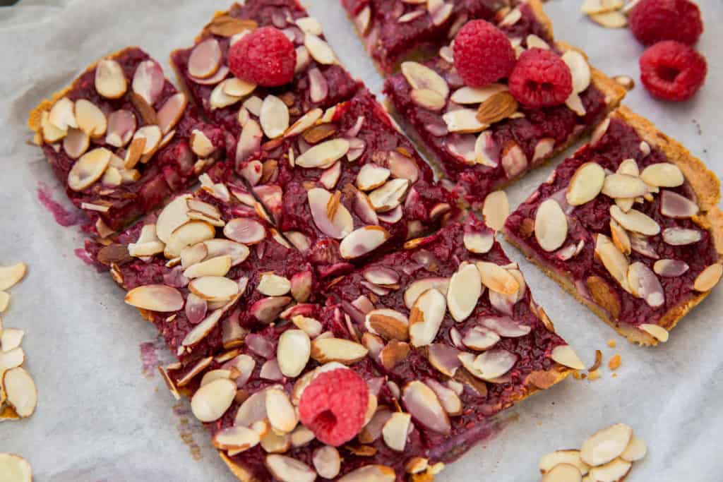 Raspberry pie bars sliced into nine bars on top of parchment paper topped with fresh raspberries