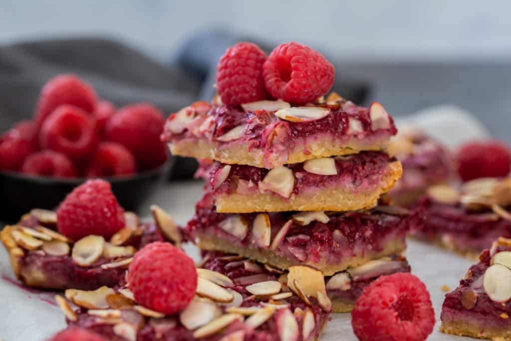 a stack of raspberry pie bars topped with fresh raspberries and surrounded by more raspberry pie bars