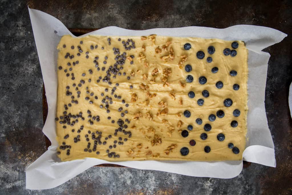 a parchment paper line sheet pan with pancake batter, blueberries, pecans and sugar free chocolate chips on top