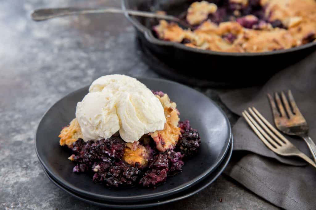 keto blackberry cobbler served on a black plate with a scoop of vanilla ice cream on top