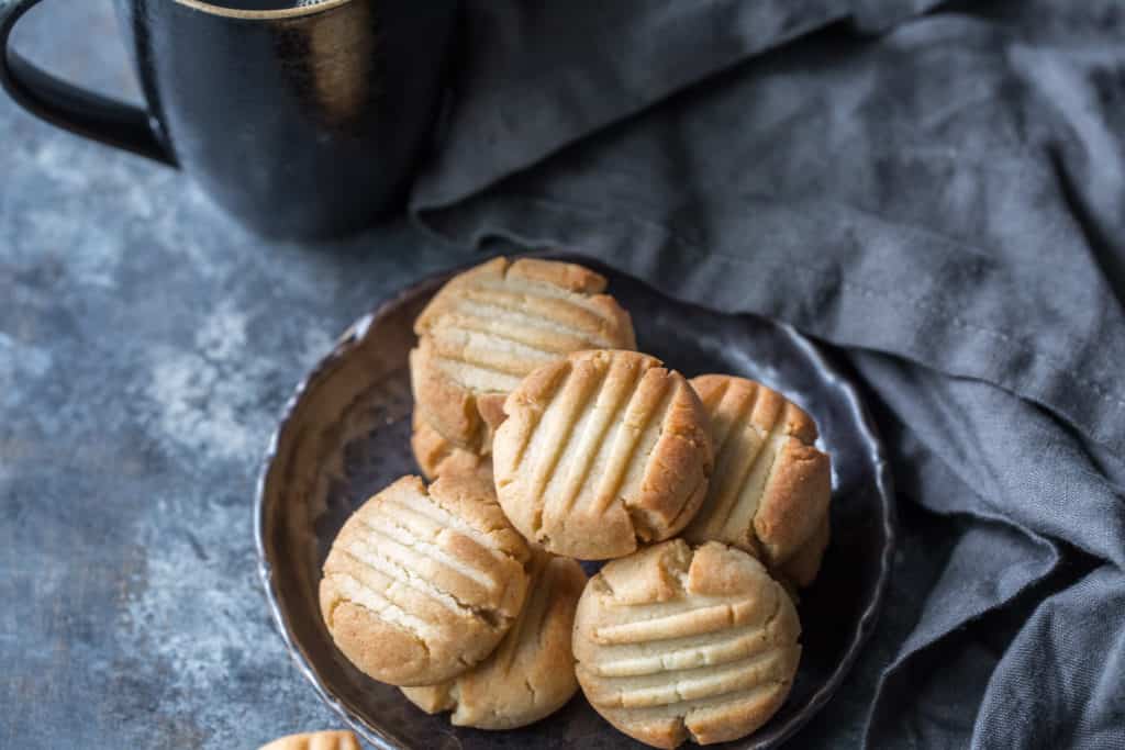 A plate of keto butter cookies next to a tablecloth and coffee