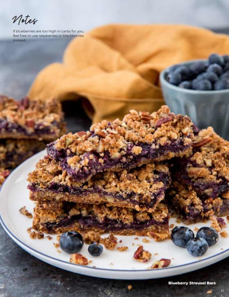 blueberry streusel bars displayed on a plate in front of a bowl of blueberries