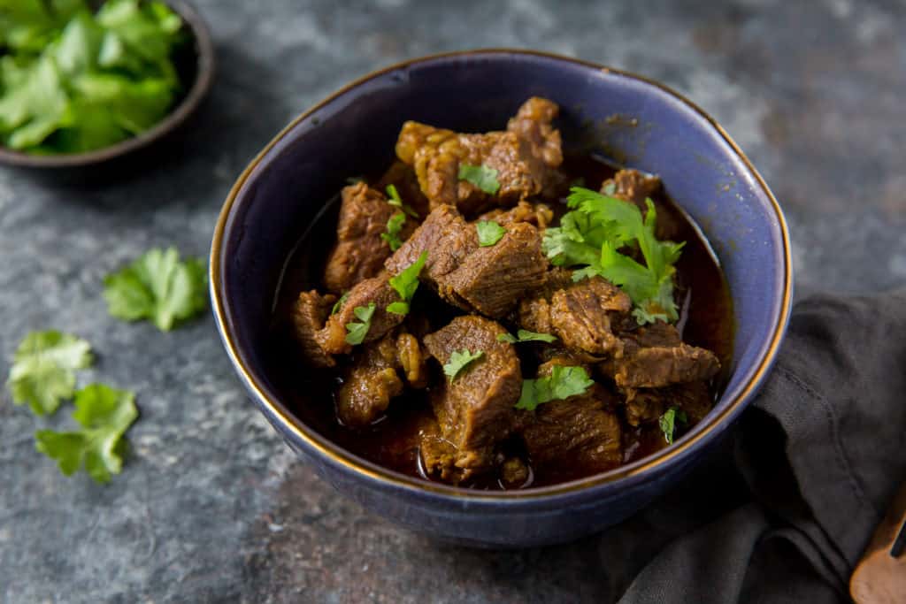 beef curry served in a blue bowl with a garnish of cilantro