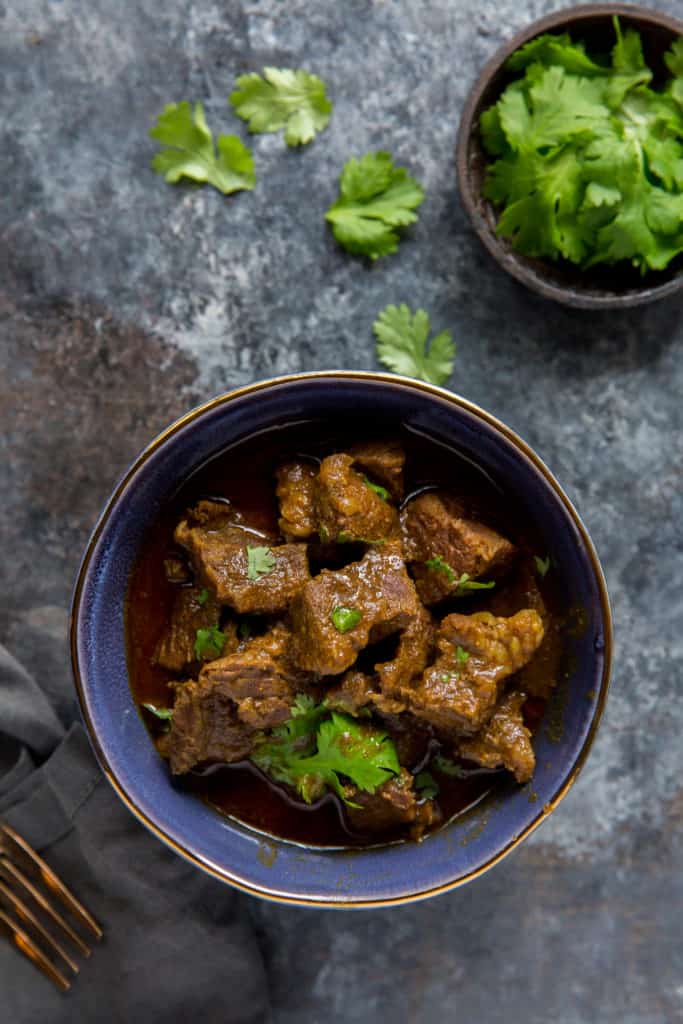 beef curry served in a blue bowl with a garnish and bowl of cilantro