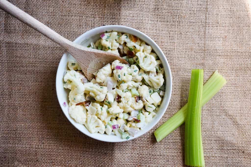 dairy free keto cauliflower salad in a white bowl being served with a wooden spoon