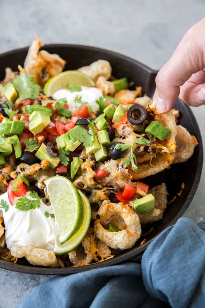 A hand reaching for keto pork rind nachos