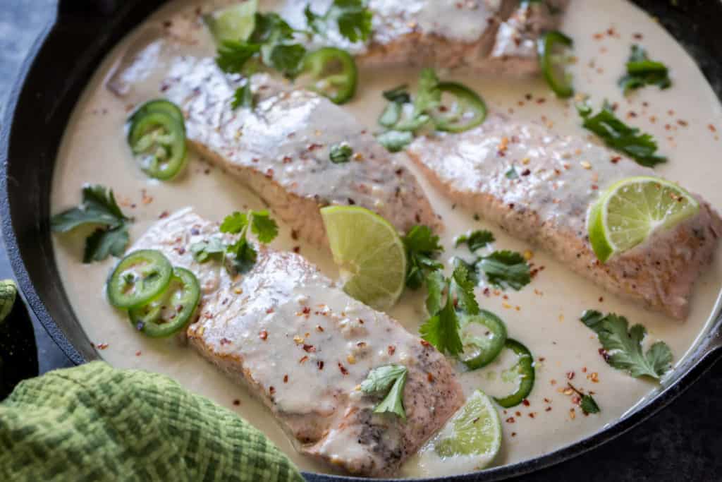 keto salmon curry in a cast iron skillet garnished with jalapenos and lime wedges