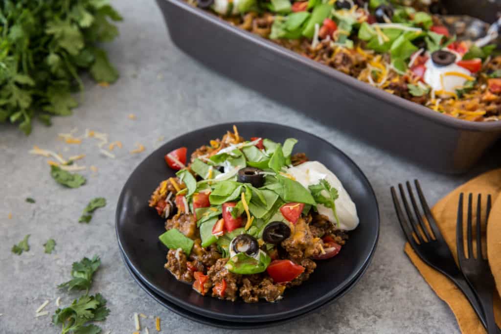 keto taco salad casserole served on a black plate garnished with lettuce, cheese, olives and sour cream