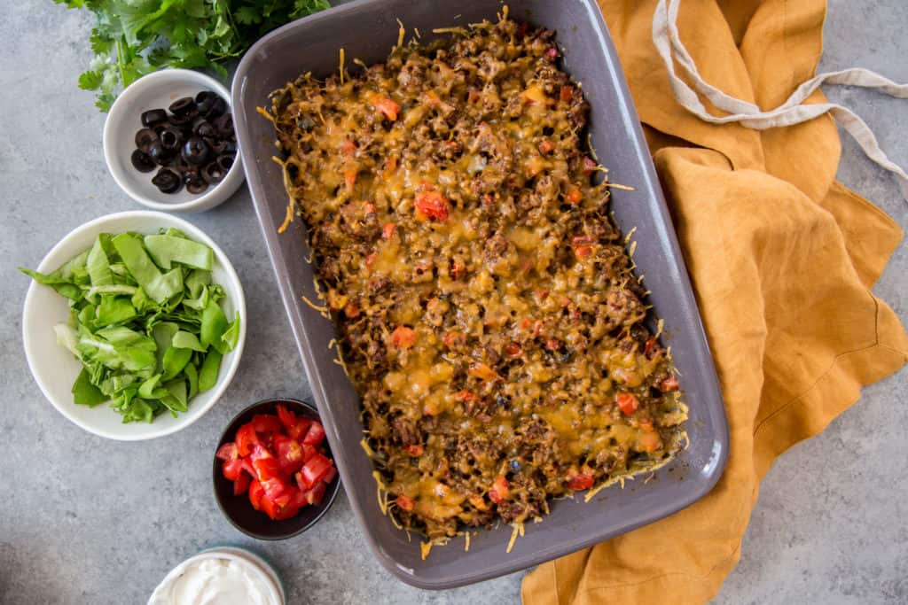 Keto Taco Salad cooked keto taco salad casserole in a casserole dish with toppings on the side