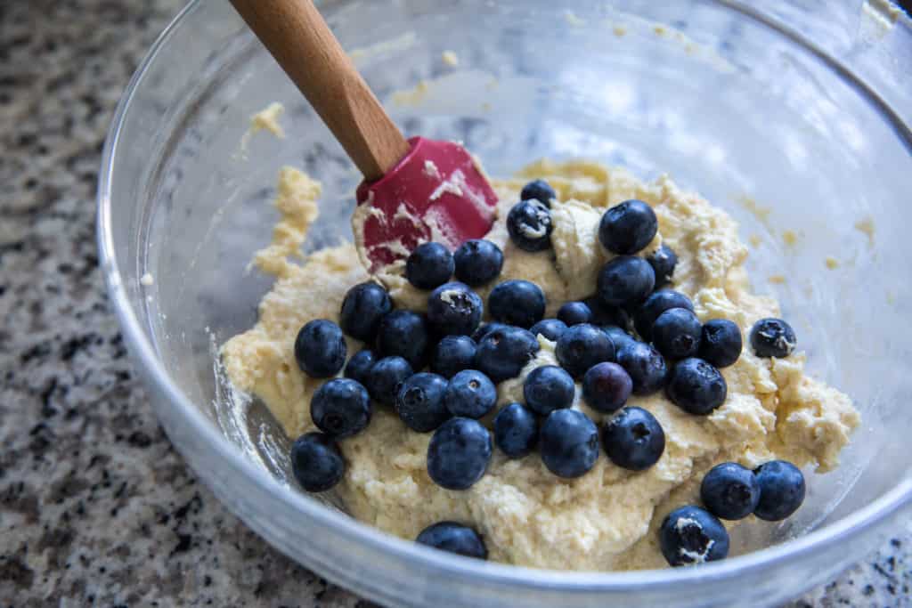a glass bowl with batter for coconut flour cocokies topped with fresh blueberries and a spatula