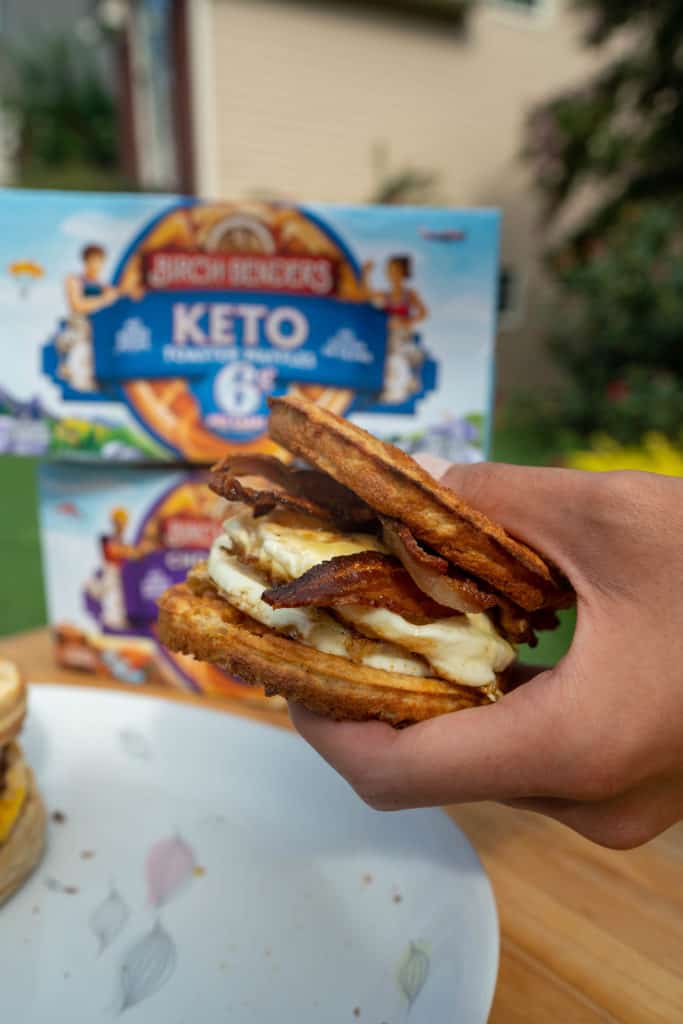 one keto breakfast sandwich held in front of a birch benders toaster waffles box