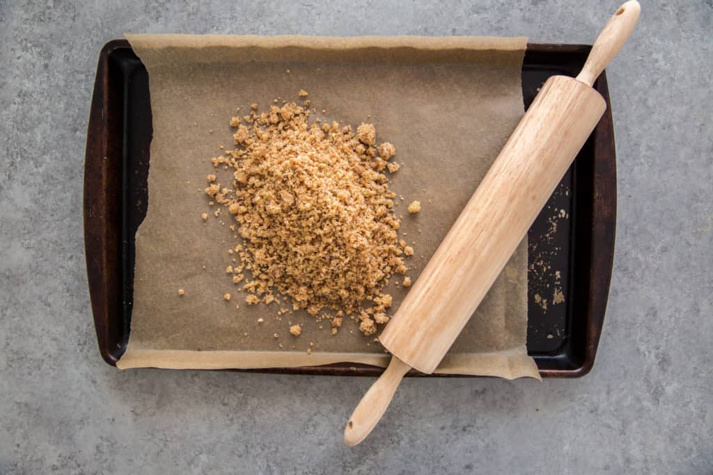 Graham cracker crumbs on a baking tray with a rolling pin