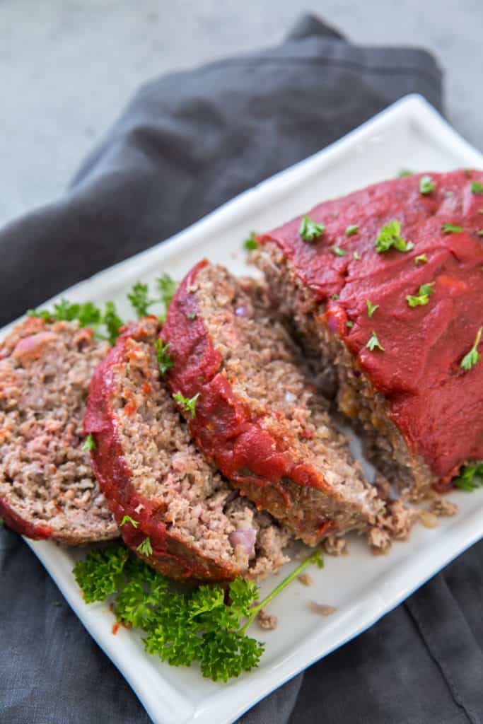 cooked keto meatloaf served on a white platter garnished with parsley and sliced