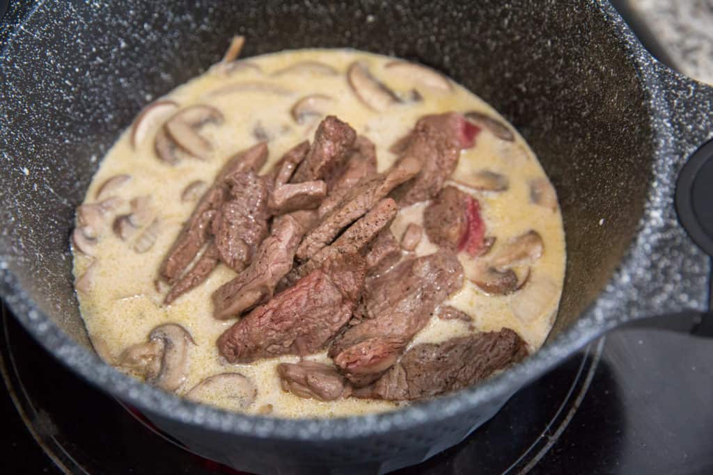 keto beef stroganoff cooking in a skillet with a cream sauce and sliced ribeye steak