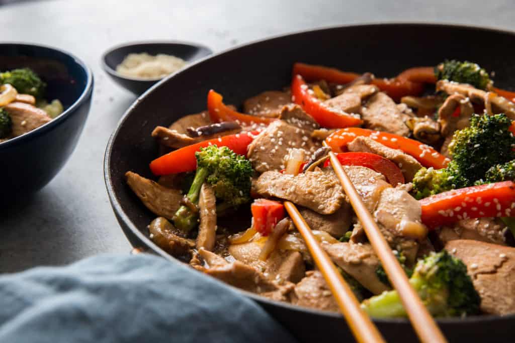 keto chicken stir fry in a large frying pan with chopsticks and cauliflower rice