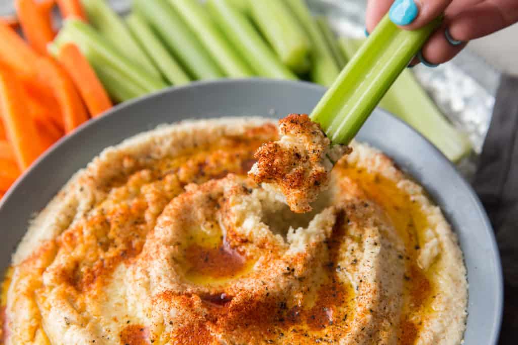 celery being dipped into a bowl of cauliflower hummus