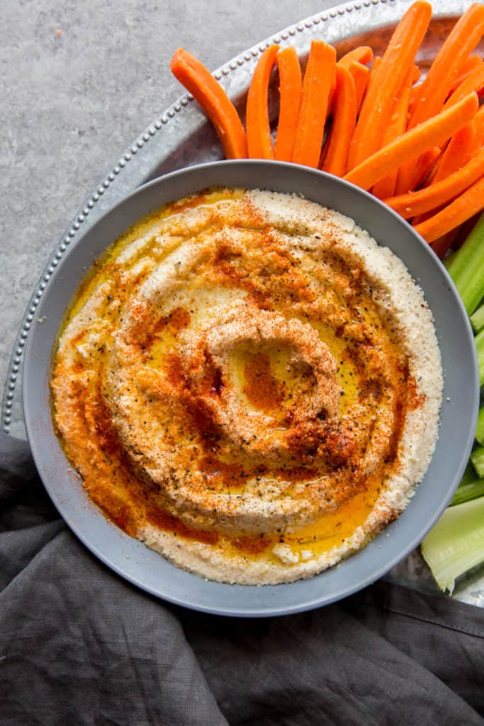 A bowl of keto hummus next to carrots and celery