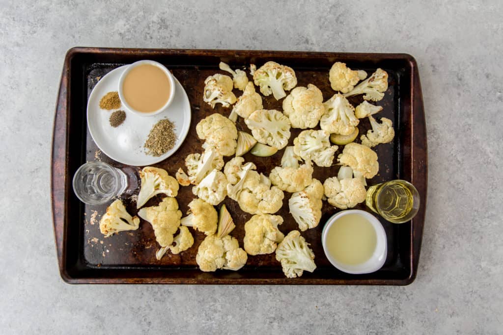 roasted cauliflower and garlic on a baking sheet with olive oil, tahini and seasonings