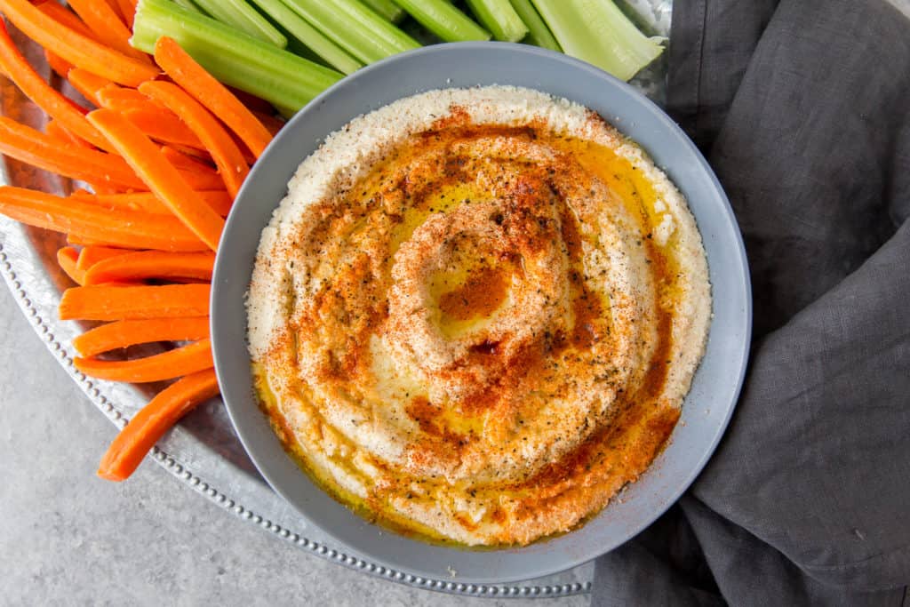 easy cauliflower hummus serve in a gray bowl on a tray with celery and carrots