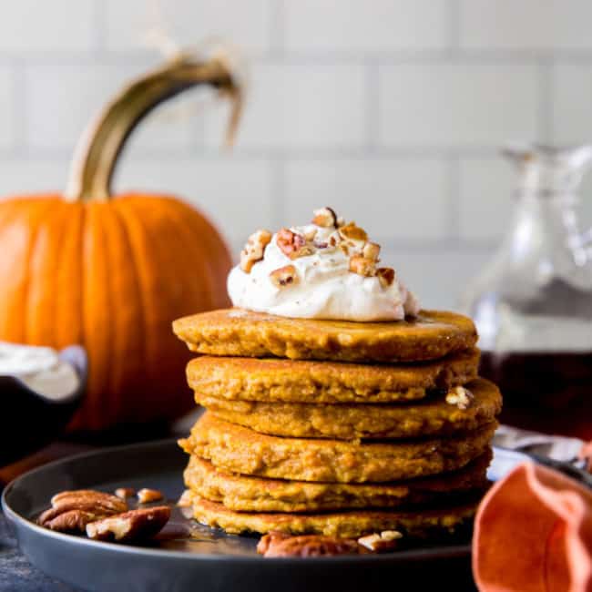 plate of pancakes with toppings and pumpkin in the background