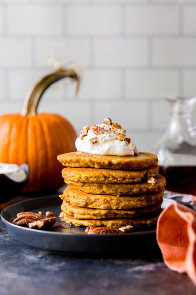 plate of pancakes with toppings and pumpkin in the background