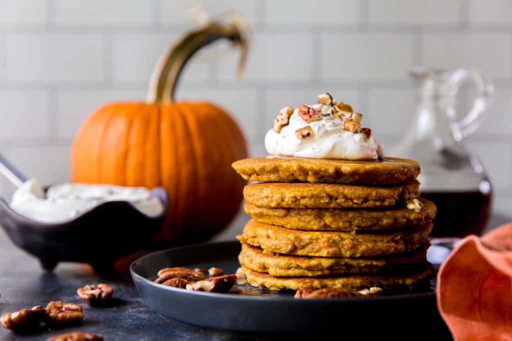 Pancake impilati con panna montata e zucca sullo sfondo