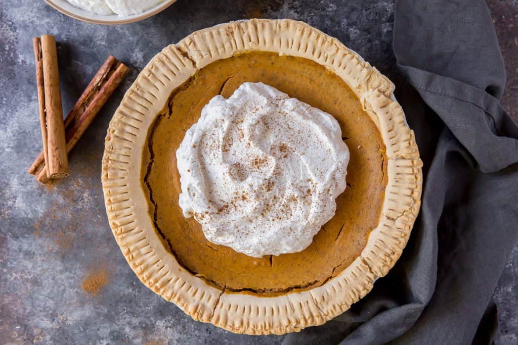 whipped topping and cinnamon stick around pumpkin pie