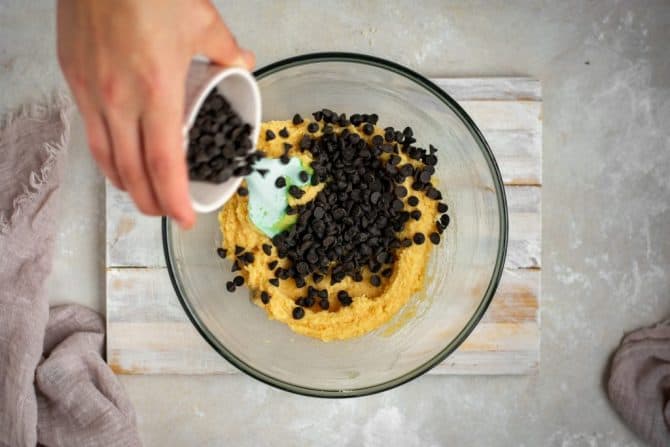 Keto Chocolate Chip Cookies Sprinkling in chocolate chips to the batter in a glass mixing bowl
