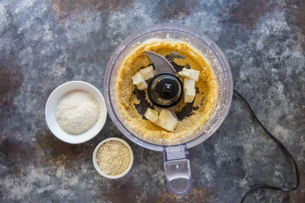 Butter being added to the food processor next to remaining ingredients