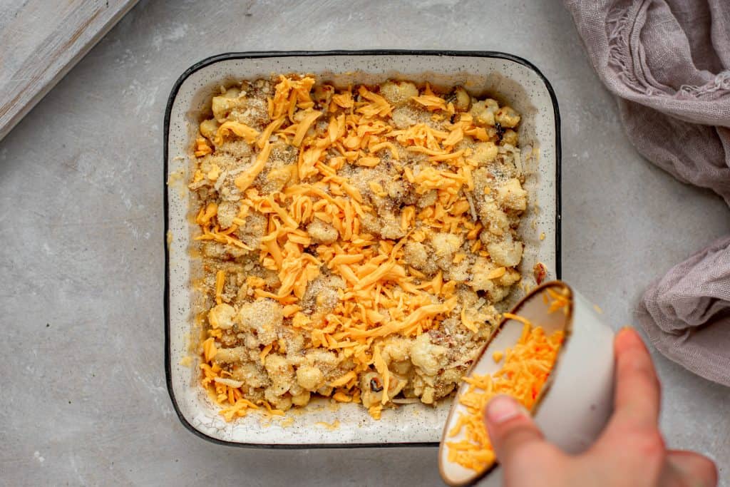 Cauliflower Mac and Cheese A ceramic bowl of cheese being sprinkled overtop of the cauliflower