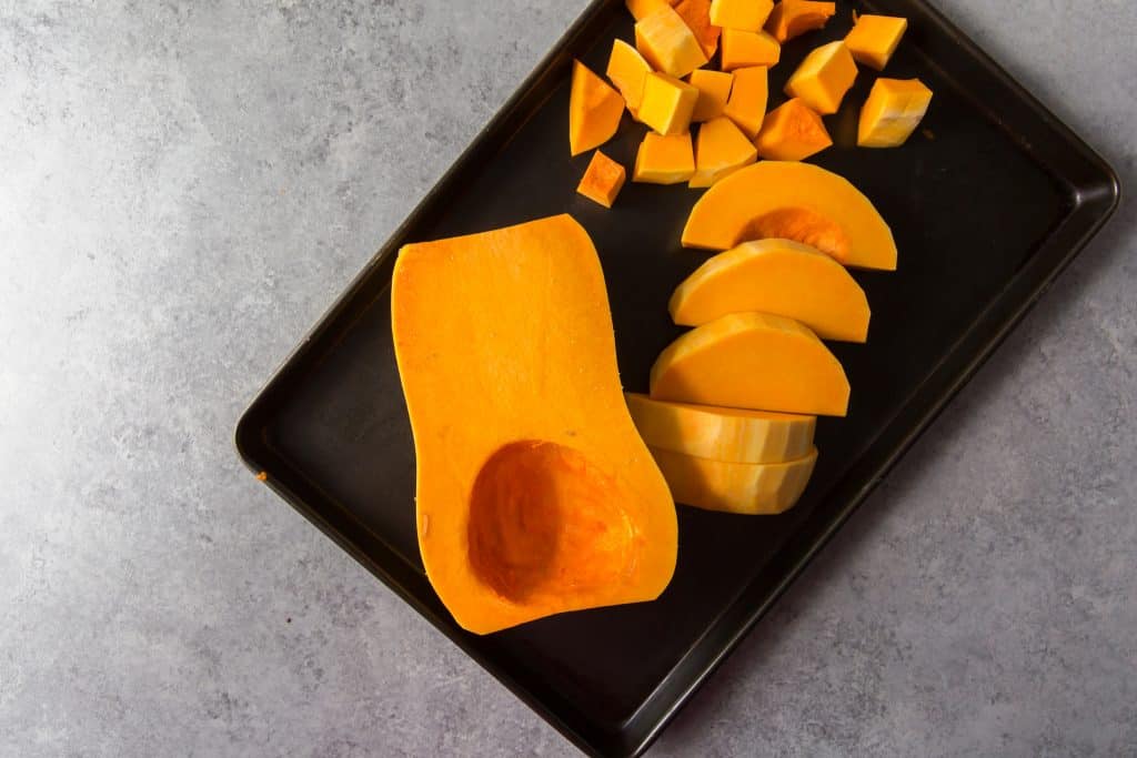 Chopped fresh butternut squash on a stainless steel baking tray