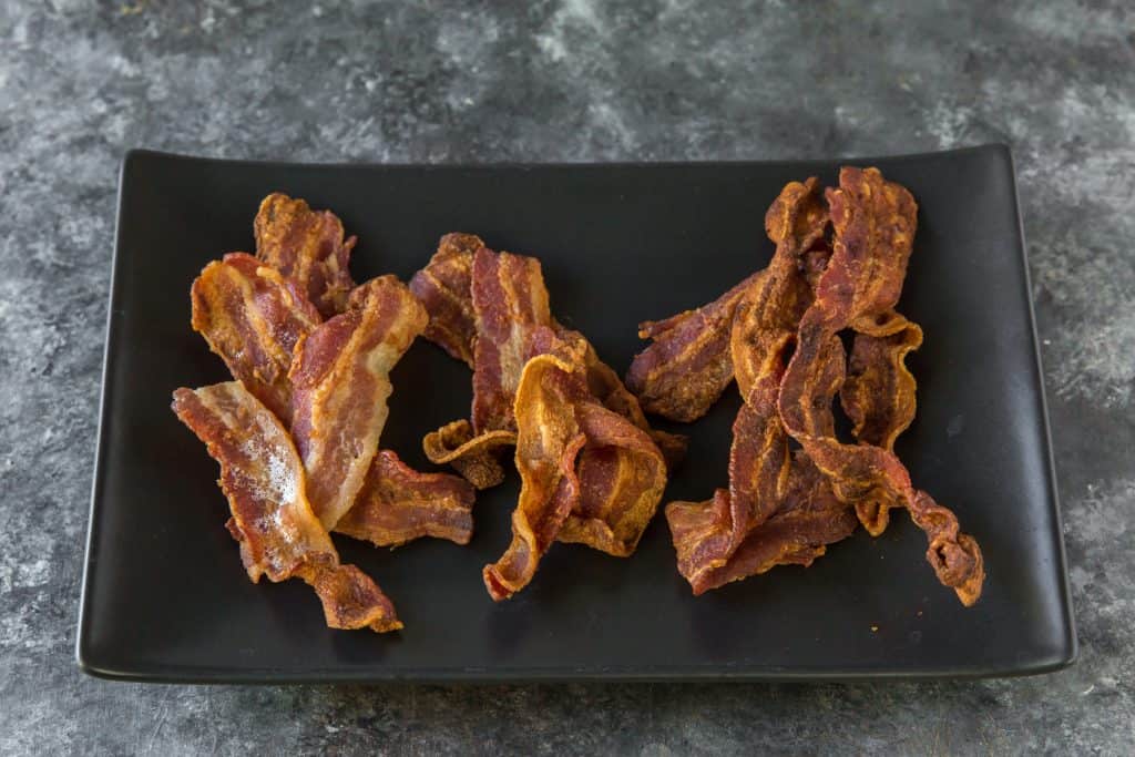 Cooked air fryer bacon on a black plate 