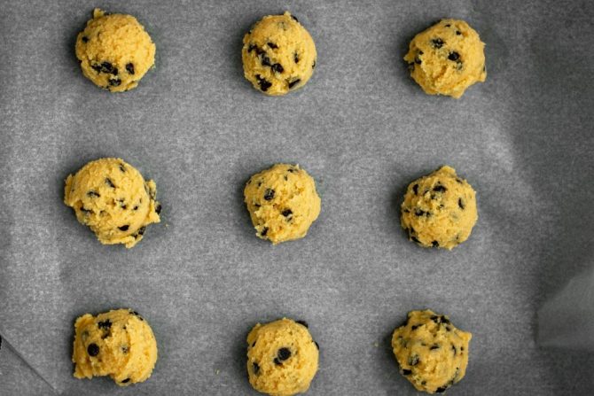 A baking sheet lined with parchment paper. Fresh cookie dough on top to be baked