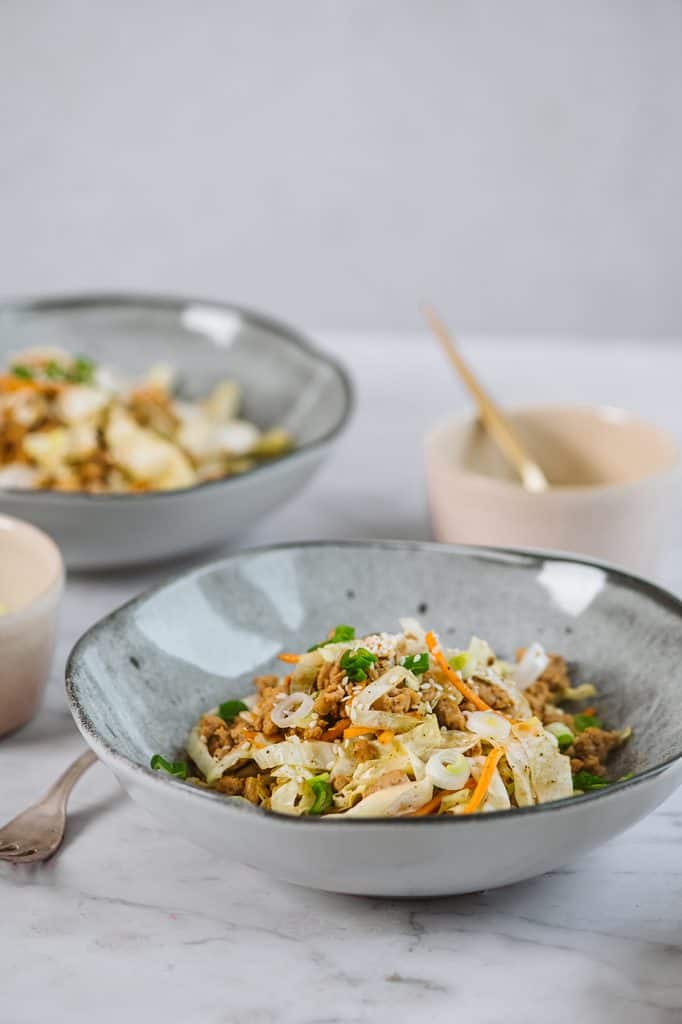 Plated egg roll in a bowl next to a fork on a marble tabletop 