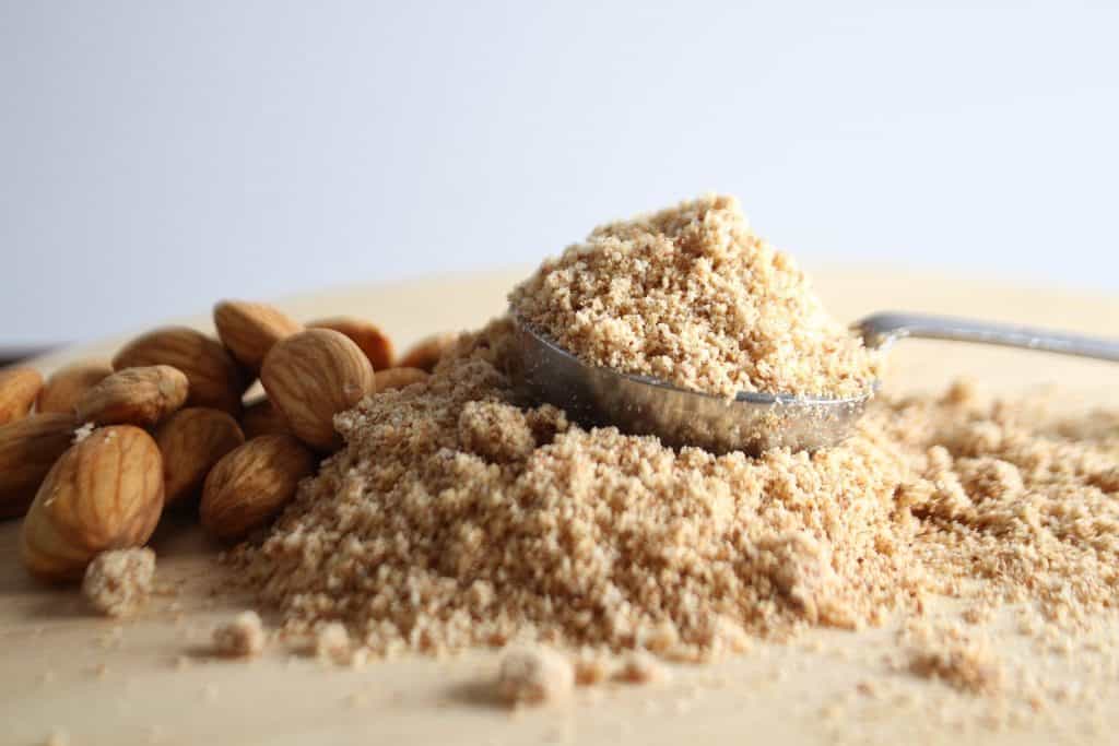 A measuring cup filled with flour with nuts in the background