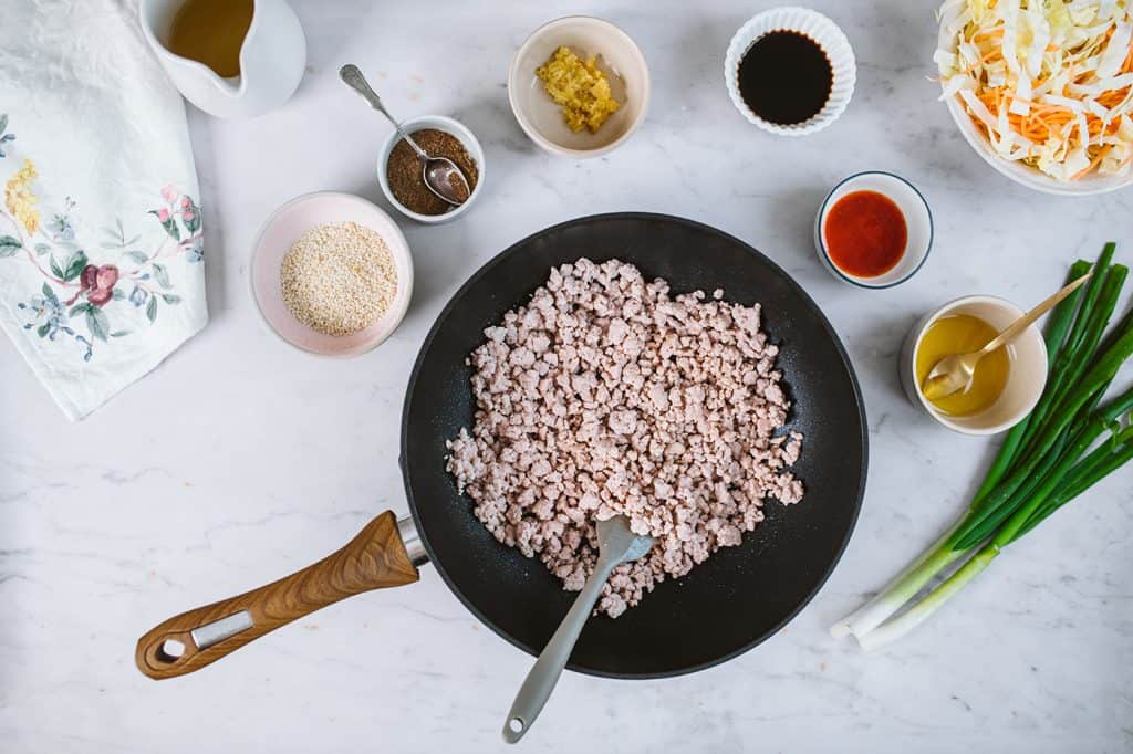 Keto Egg Roll In A Bowl A pan with freshly cooked pork surrounded by spring onions, sesame oil, and spices