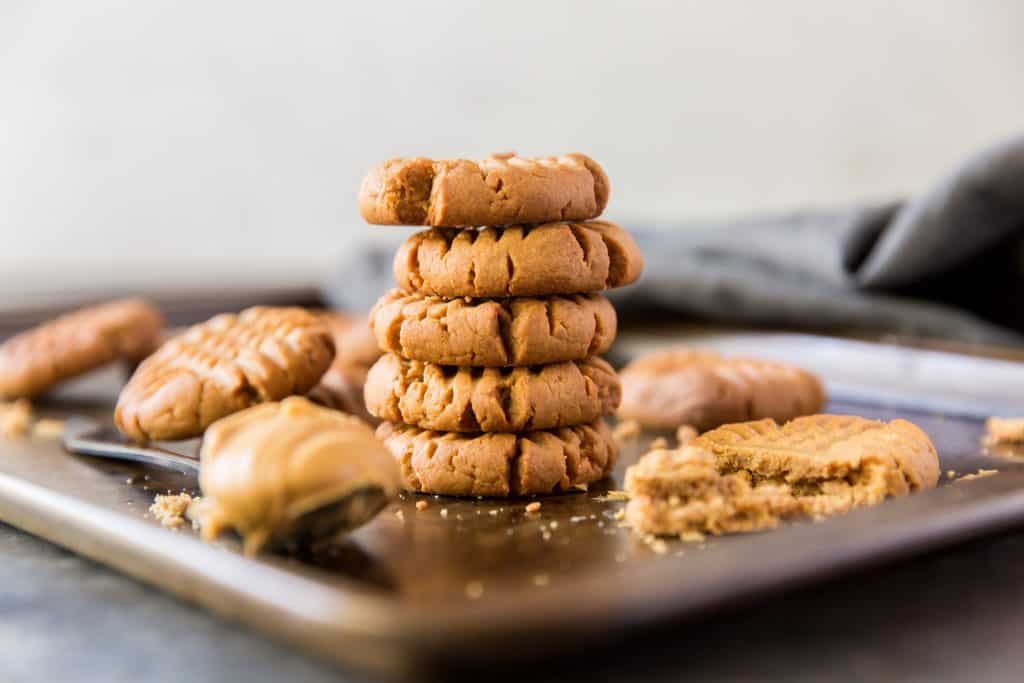 Keto Peanut Butter Cookies Cookies stacked on a baking sheet next to peanut butter